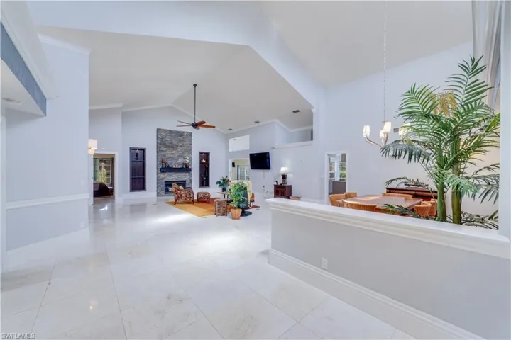 Living room featuring Polished Travertine marble floors, a stone fireplace, ornamental molding, and high vaulted ceiling
