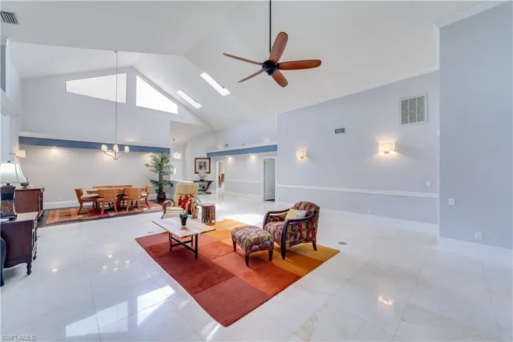 Living room with a high ceiling, ceiling fan with notable chandelier, a stone fireplace, and crown molding