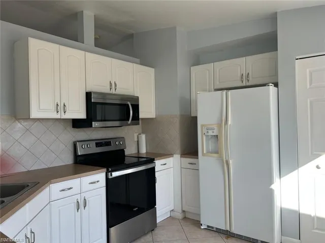 Kitchen with appliances with stainless steel finishes, dark countertops, light tile patterned floors, and white cabinetry