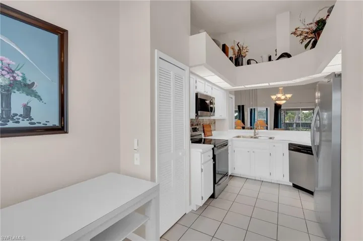 Kitchen with stainless steel appliances, white cabinetry, light countertops, light tile patterned floors, and a high ceiling