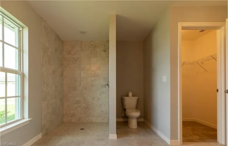 Full bath with a spacious closet, tiled shower, and light tile patterned floors