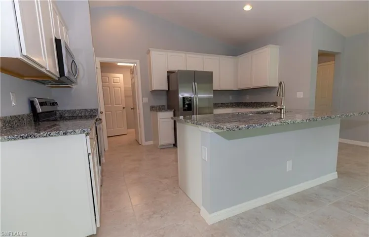 Kitchen featuring white cabinetry, lofted ceiling, dark stone counters, stainless steel appliances, and recessed lighting