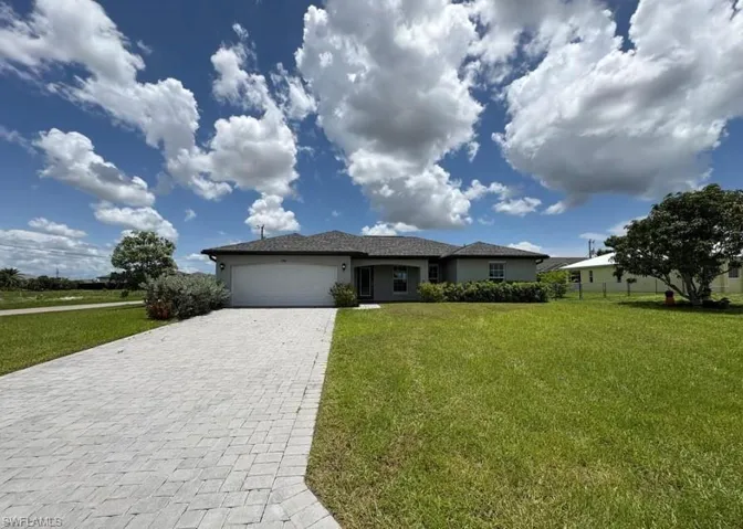 Ranch-style home featuring a front lawn, a garage, decorative driveway, and stucco siding
