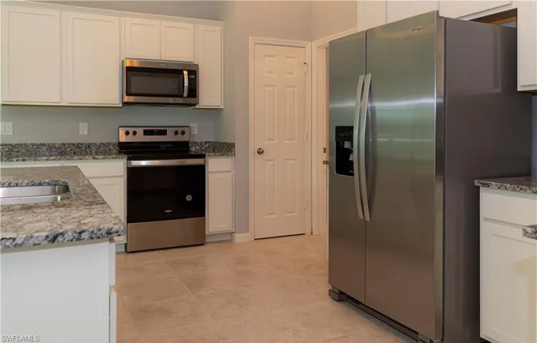 Kitchen with stainless steel appliances, light stone counters, and white cabinets