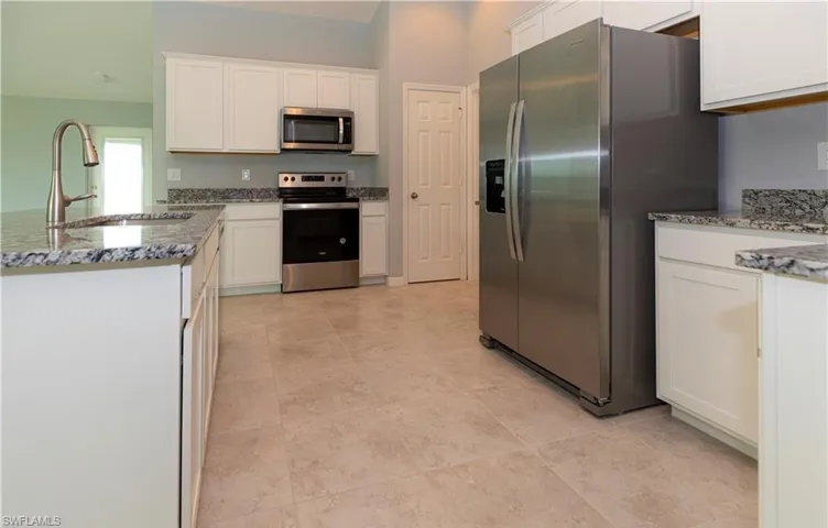 Kitchen featuring light stone counters, stainless steel appliances, white cabinetry, and a peninsula