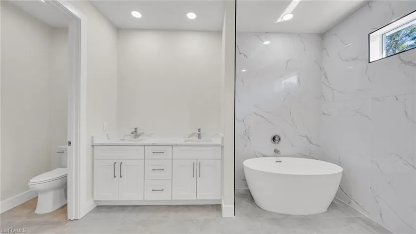 Full bathroom with a soaking tub, double vanity, recessed lighting, and tile walls