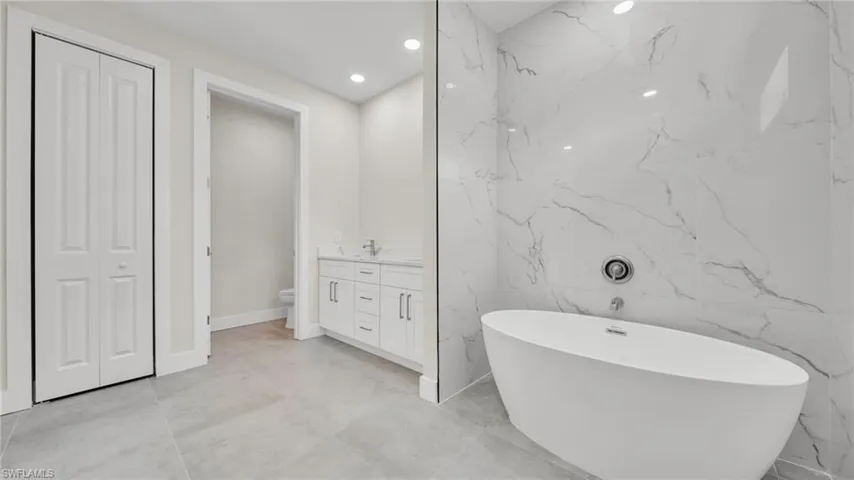 Bathroom with recessed lighting, a soaking tub, vanity, tile walls, and stone wall