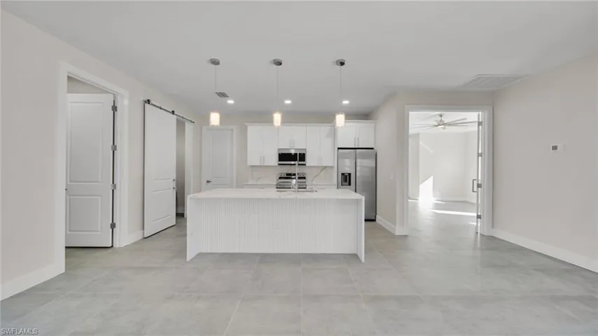 Kitchen featuring white cabinetry, an island with sink, appliances with stainless steel finishes, light stone countertops, and pendant lighting