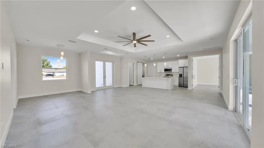 Unfurnished living room featuring ceiling fan, recessed lighting, french doors, and a tray ceiling