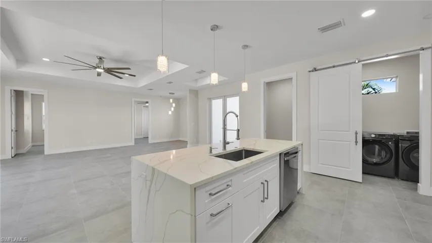 Kitchen with pendant lighting, recessed lighting, white cabinetry, light stone countertops, and washing machine and dryer