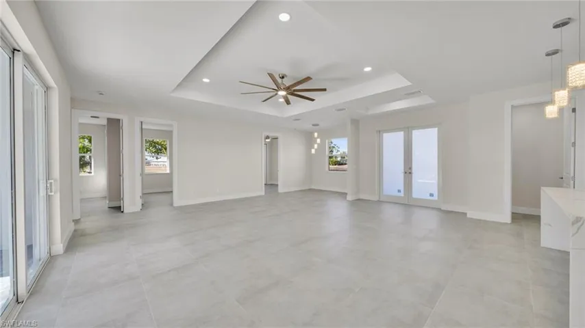 Unfurnished living room featuring french doors, recessed lighting, a ceiling fan, and a tray ceiling