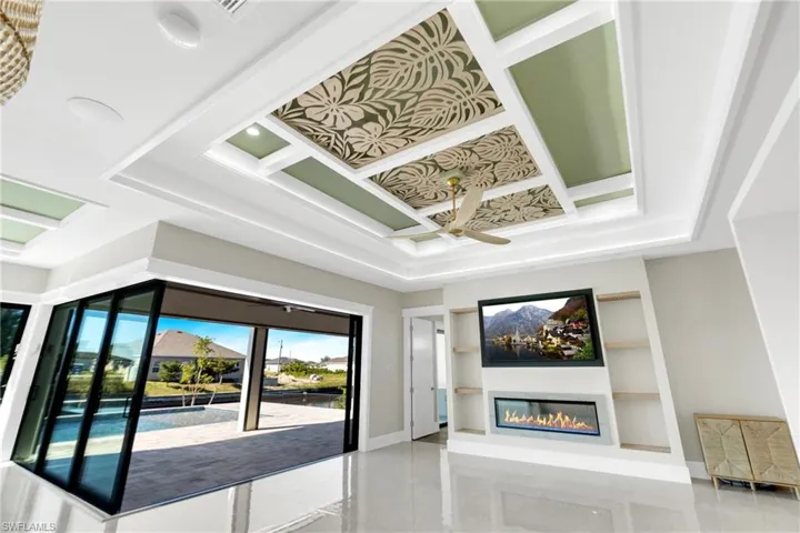 Unfurnished living room with coffered ceiling, a glass covered fireplace, built in features, and ceiling fan