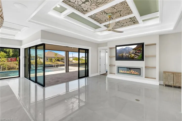 Unfurnished living room featuring a glass covered fireplace, built in shelves, coffered ceiling, a ceiling fan, and a raised ceiling