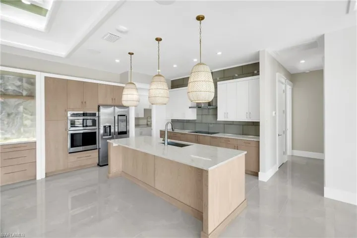 Kitchen featuring light stone countertops, decorative light fixtures, light brown cabinetry, stainless steel appliances, and modern cabinets