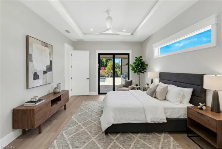 Bedroom featuring wood finished floors, access to exterior, and a tray ceiling