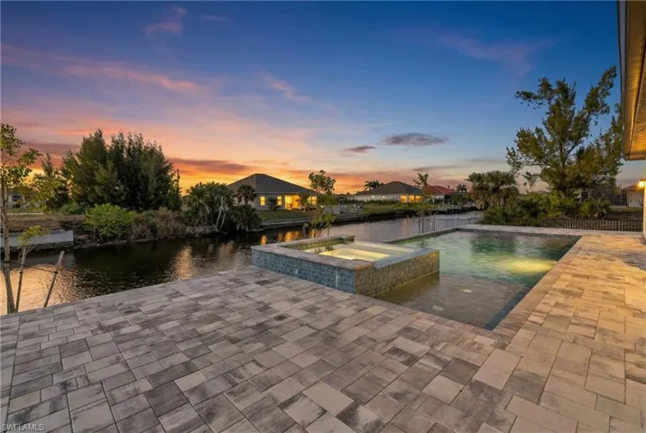 Pool at dusk featuring a patio, a water view, and a pool with connected hot tub