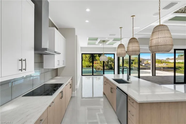 Kitchen with light stone counters, decorative light fixtures, wall chimney exhaust hood, light brown cabinets, and stainless steel dishwasher