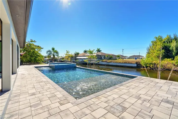 View of pool featuring a patio area, a pool with connected hot tub, a water view, and a residential view