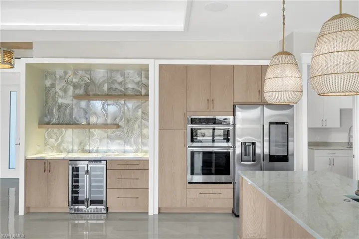Kitchen with decorative light fixtures, light stone counters, beverage cooler, appliances with stainless steel finishes, and modern cabinets