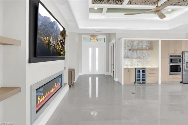 Unfurnished living room featuring beverage cooler, ceiling fan, french doors, a glass covered fireplace, and a tray ceiling