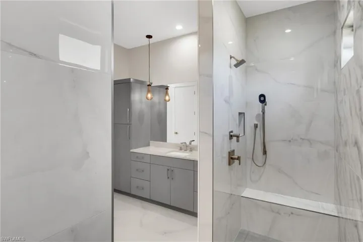 Bathroom with vanity, a marble finish shower, and light marble finish flooring