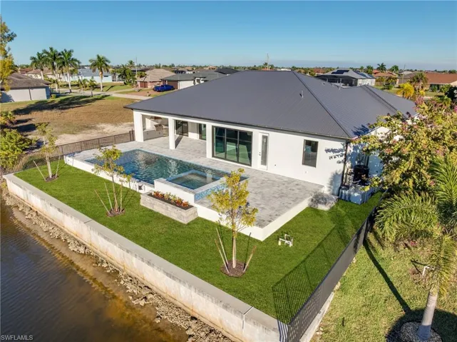 Rear view of house with a fenced backyard, a patio, a residential view, a metal roof, and an in-ground hot tub