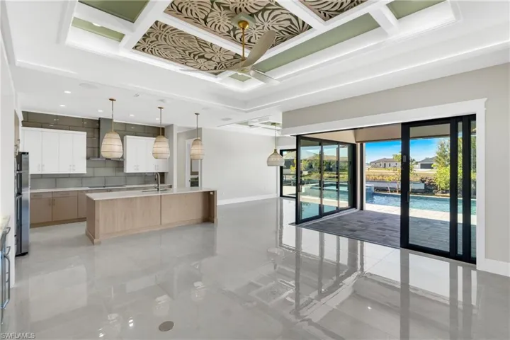 Kitchen featuring white cabinets, open floor plan, ceiling fan, a kitchen island with sink, and decorative light fixtures
