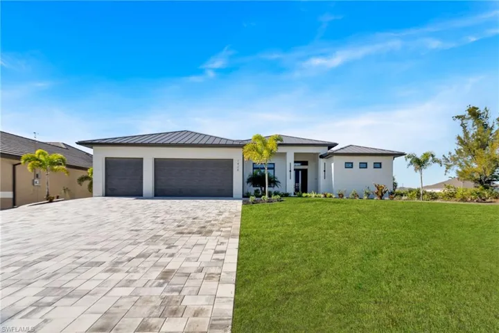 Prairie-style house with a front lawn, a metal roof, decorative driveway, and stucco siding