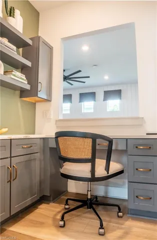 Built-in desk area featuring grey cabinetry with gold-tone hardware, a light-toned countertop, and wood-finish flooring