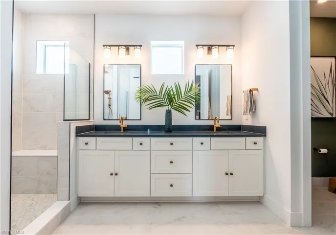Double vanity featuring white shaker-style cabinetry, dark countertops, and gold-toned fixtures