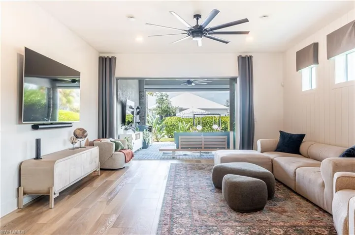 Living area featuring wood-finish flooring, a contemporary ceiling fan, recessed lighting, and sliding glass doors leading to an outdoor patio with lush landscaping