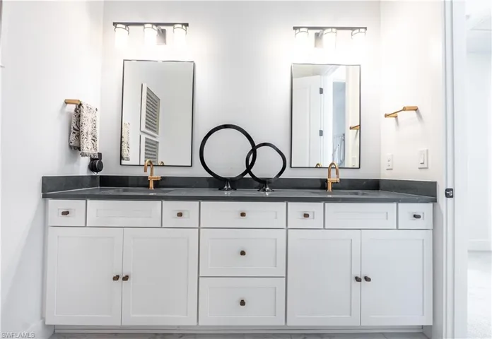 Dual vanity featuring a dark countertop, two undermount sinks with gold-toned faucets, white shaker-style cabinetry, and two rectangular mirrors with black frames