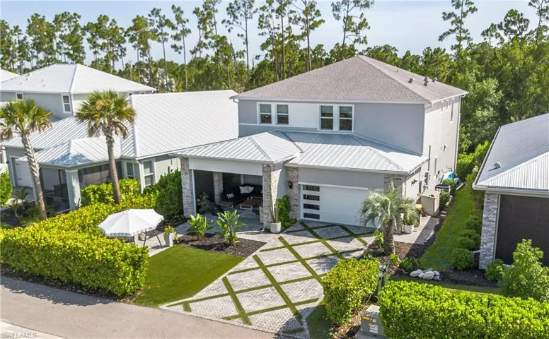 Modern-style residence featuring a patterned paver driveway, an attached garage with a contemporary door, a covered entry with stone accents, a landscaped front yard with artificial turf, and mature hedge borders