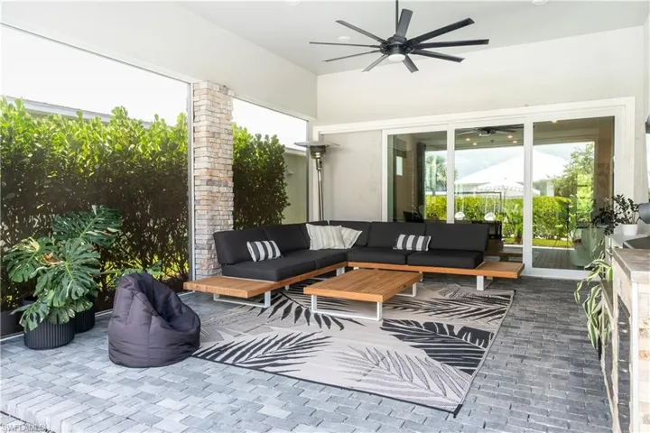 Covered patio featuring a large ceiling fan, stone-clad pillar, and gray paver flooring