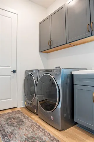 Utility room featuring laundry sink, wood-finish flooring, white walls, and built-in gray cabinetry with gold-tone hardware