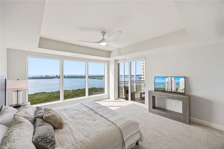 Carpeted bedroom featuring a tray ceiling, access to outside, multiple windows, and ceiling fan