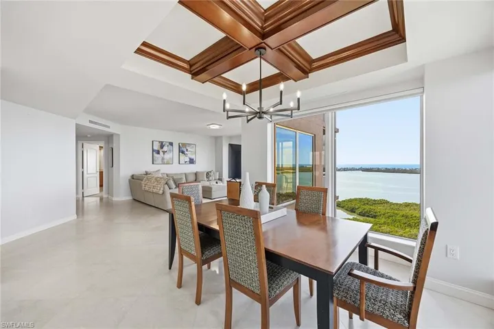 Dining space with coffered ceiling, a water view, a chandelier, and beam ceiling