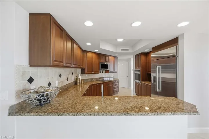 Kitchen featuring light stone counters, stainless steel appliances, backsplash, recessed lighting, and a tray ceiling