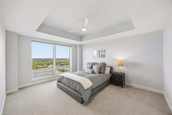 Bedroom with ceiling fan, light carpet, and a raised ceiling