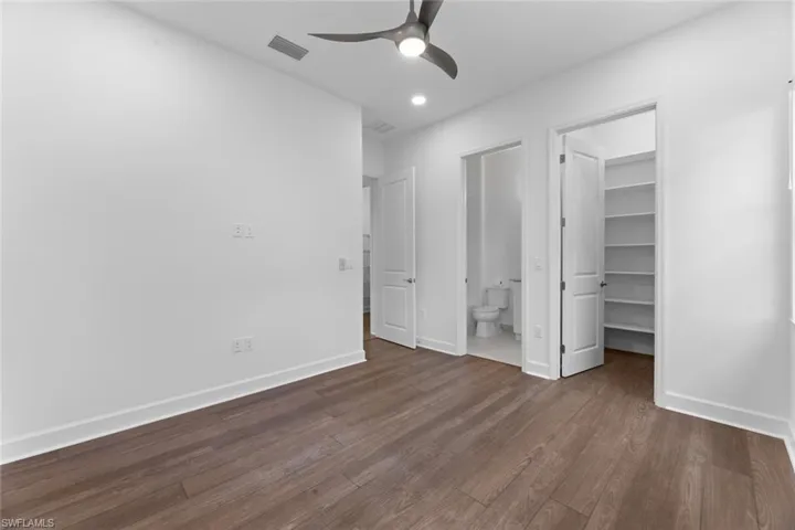 Unfurnished bedroom with ensuite bath, a spacious closet, wood-type flooring, and ceiling fan