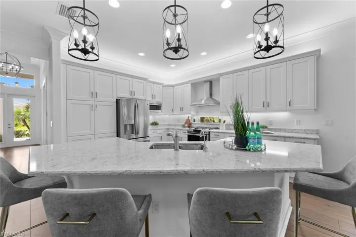 Kitchen featuring stainless steel appliances, wall chimney range hood, sink, light hardwood / wood-style floors, and a spacious island