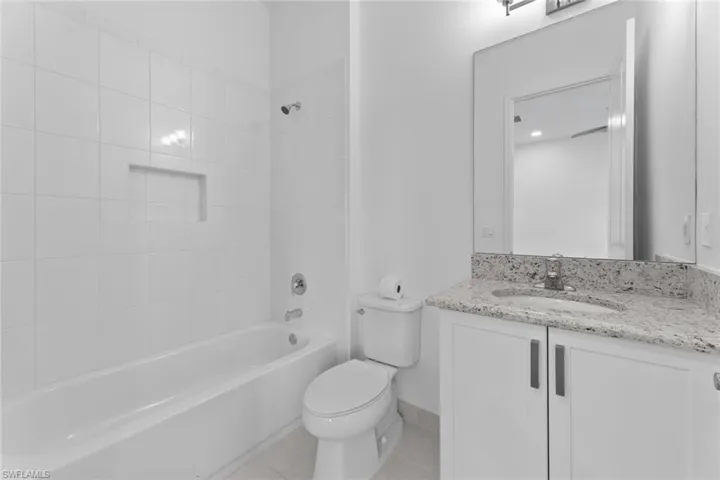 Guest ensuite Full bathroom with tile patterned flooring, toilet, vanity, and tiled shower / bath