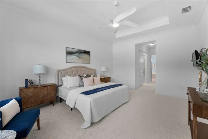 Bedroom with light colored carpet, connected bathroom, ceiling fan, and a tray ceiling, room for seating area