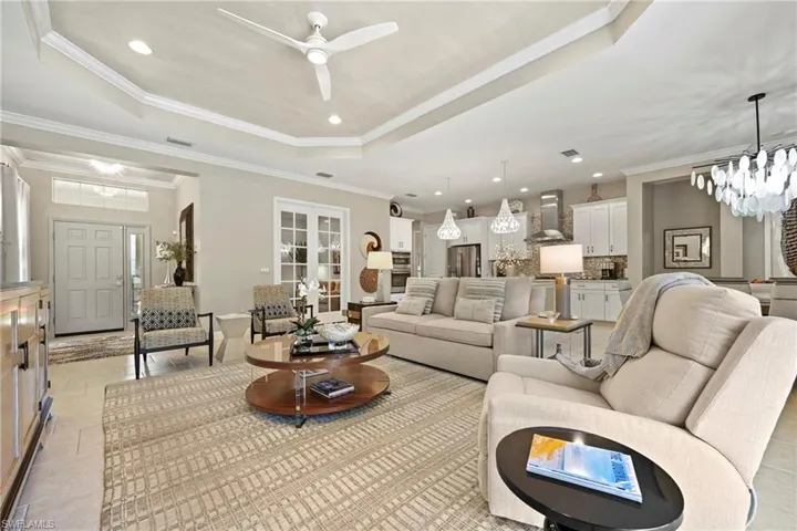 Living area with a chandelier, a raised ceiling, recessed lighting, ornamental molding, and light tile patterned flooring