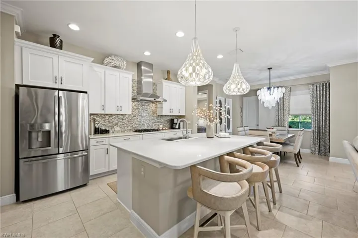 Kitchen with stainless steel fridge with ice dispenser, white cabinets, wall chimney exhaust hood, hanging light fixtures, and a chandelier
