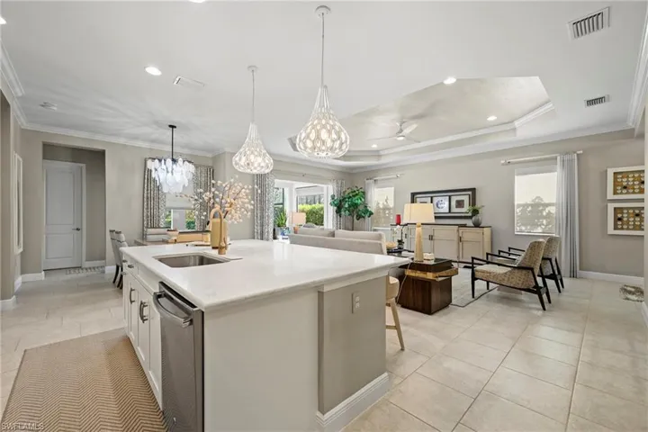 Kitchen with white cabinetry, ornamental molding, pendant lighting, stainless steel dishwasher, and light stone counters