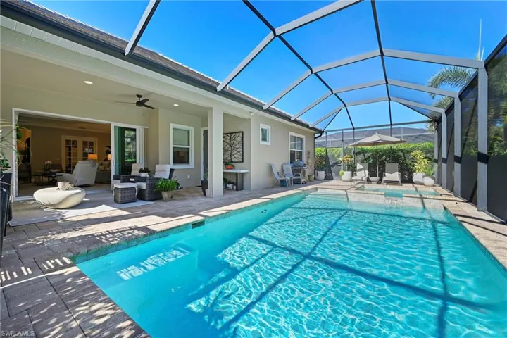 View of pool featuring a patio area, a sunroom, glass enclosure, a grill, and a pool with connected hot tub