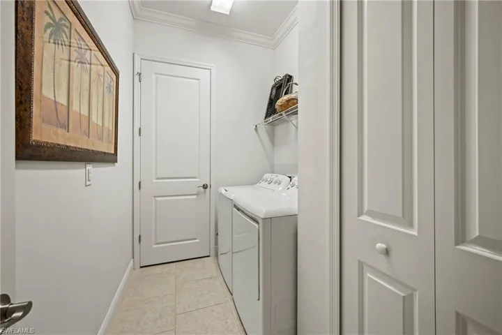 Laundry room with crown molding, independent washer and dryer, and light tile patterned floors