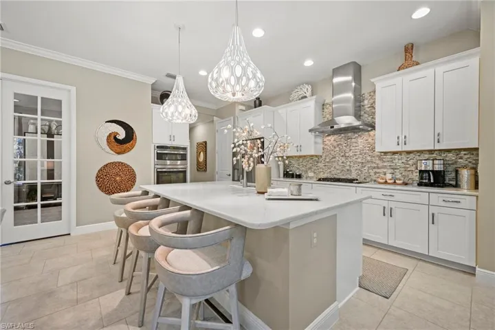 Kitchen with hanging light fixtures, an island with sink, a kitchen bar, white cabinets, and ornamental molding