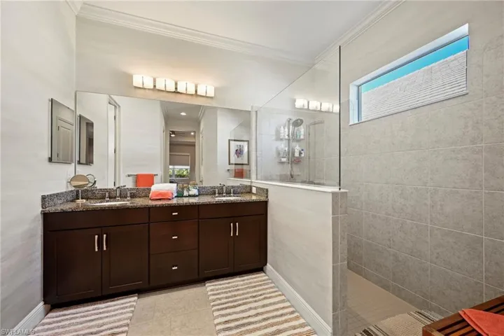 Bathroom with double vanity, crown molding, a walk in shower, healthy amount of natural light, and light tile patterned floors